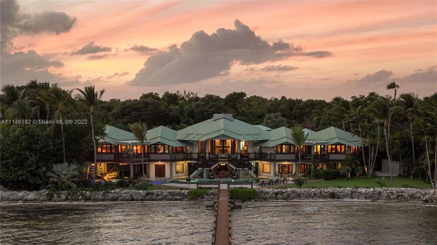 Bali Hai ~ Located in Islamorada in the incomparable Florida Keys, you will find this extraordinary, secluded estate on almost 4 oceanfront acres and over 200 feet on the ocean. At the entrance, you are greeted by the artistically created one-of-a-kind gate; you then follow a winding, magical private drive surrounded by lush foliage and highlighted at night with beautiful landscape lighting. As you approach the home, you will be entranced by this Balinese-influenced architecturally designed home, highlighted by its pitched, flared roofs and exposed trusses together with magnificent round columns adorned in lustrous green riverbed stone imported from East Timor and Bali. These elements and designs are intended to balance the natural beauty surrounding the home inside and out.
