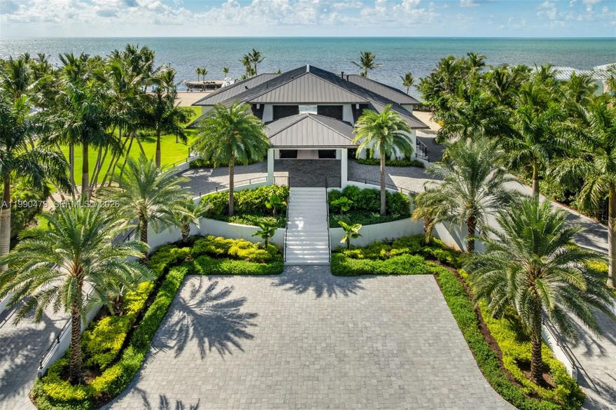 A private sanctuary of coastal sophistication, The Oasis offers two residences spanning 2.85 meticulously landscaped acres with over 400 feet of pristine waterfront and a protected deepwater basin. Designed for elevated living, The Oasis blends resort-style amenities with the privacy and scale of a true Florida Keys compound. The grand porte-cochère entry sets the tone, leading to a single-level main residence with soaring ceilings, white oak floors, and 12' retractable glass walls that frame sweeping ocean views. The chef's kitchen is anchored by a Calacatta marble island, Thermador appliances, and a walk-in pantry, opening to a spacious great room and dining area ideal for entertaining. The main home features four bedrooms, six full bathrooms, and a soundproof theater. The primary suite is a private retreat with a fireplace, dual walk-in closets, a safe room, and a spa-inspired bath with a steam shower. Each additional bedroom includes an en suite bath, private balcony, and ocean views. A detached guest house offers two additional bedrooms and bathrooms, creating a total of six bedrooms across the estate with endless space for expansion. The summer kitchen, alfresco dining areas, and multiple lounging terraces offer seamless indoor-outdoor living. The deepwater basin accommodates larger vessels. Amenities rival a private resort: soundproof theater, fitness center with sauna, golf simulator, and two resort-style pools—each with a spa, sun deck, & outdoor entertaining spaces.