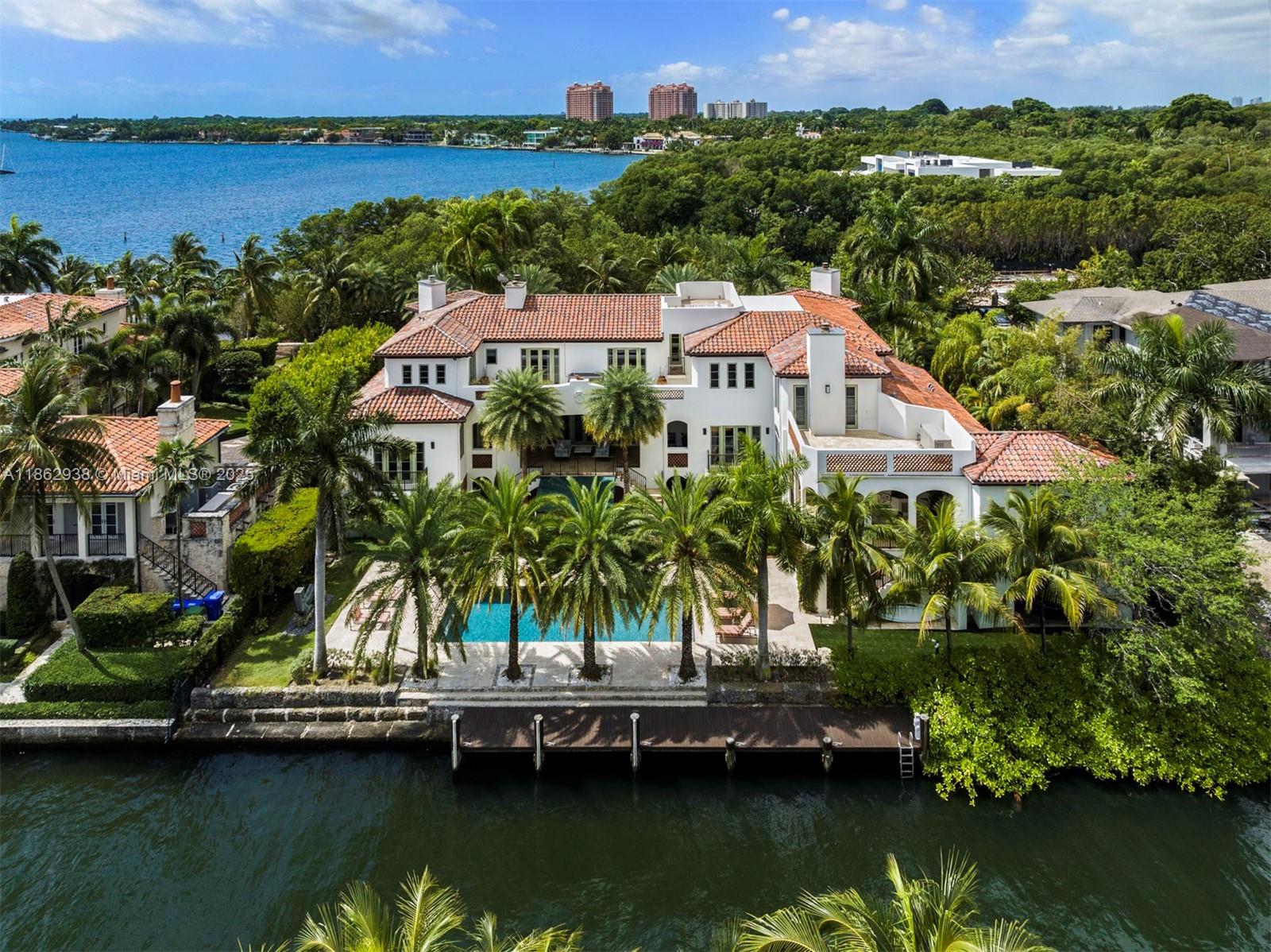 Nestled in the exclusive guard-gated enclave of The Moorings, this enchanting 17,873 SF waterfront estate captures the essence of Coconut Grove living. Designed with timeless elegance, the 7BD/7+2BA home offers refined craftsmanship and spaces that flow seamlessly to sweeping bay views. Covered terraces invite year-round outdoor living, while the gourmet kitchen with its grand island is the heart of the home. The primary suite is a serene retreat with sitting area, spa-like bath, and fireplace. With 143 ft of waterfront, enjoy a sparkling pool, private dock with direct Biscayne Bay access, and a rooftop terrace for sunset vistas. Just minutes from Coconut Grove’s charming boutiques, fine dining, and top schools, this residence embodies tropical sophistication.