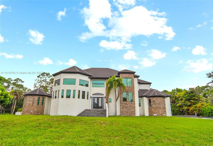 Discover one of the largest and most captivating homes in Jupiter Farms, offering over 6,000 sq ft on a lush 1.10 acre lot. With 35 foot ceilings, walls of light, and a seamless open floor plan, this estate offers luxury, comfort, and privacy. The chef’s kitchen features gas cooking, double ovens, granite, and a wine cooler. The master suite includes a spa inspired bath, walk in closet, and private balcony. Enjoy a resort style backyard with heated pool, cleared land for expansion, and no HOA. The epoxy finished garage fits a lift or indoor court. Smart tech includes zoned A/C, app controlled blinds and gate, TVs in every room, and security cameras. Perfect as a multigenerational home, luxury rental, or your forever estate, “The Castle” delivers a lifestyle like no other.