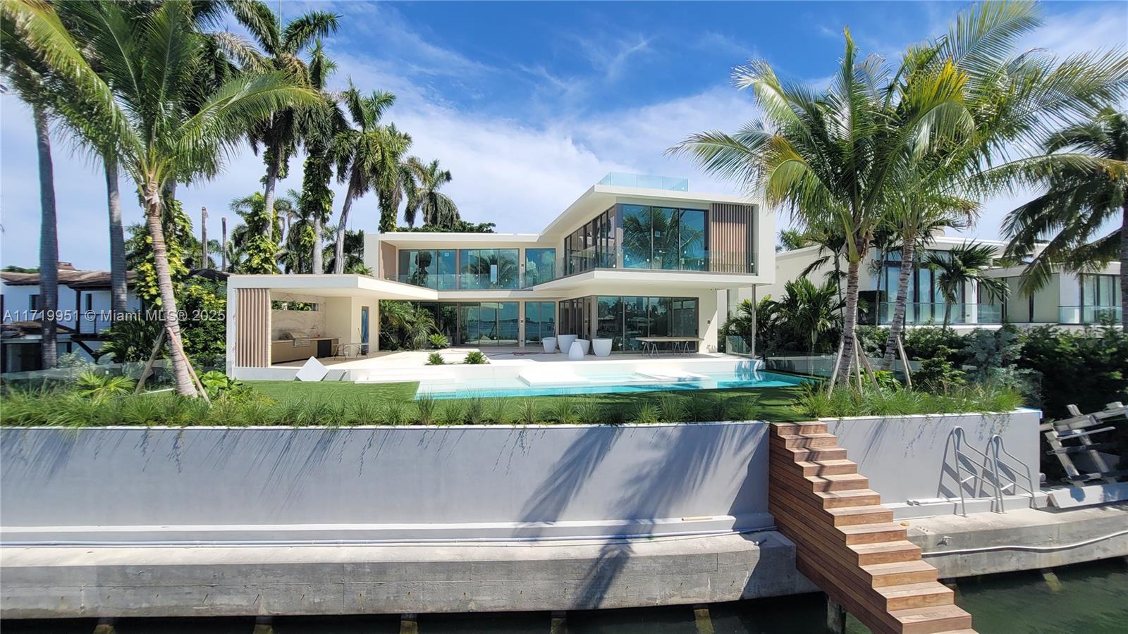 This brand-new, elevated, luxury home offers over 9,000 sqft of contemporary living with open water bay views and Miami skyline sunsets. Boasting 6 spacious bedrooms, 6 plus 2 half bathrooms, the residence features exquisite interior finishes. Custom kitchen by Ernestomeda with high-end appliances by Wolf, Miele, and Sub-Zero. Custom bathrooms by Casabath. White oak ceilings in the primary bedroom and dreamy walk-in closet, floor-to-ceiling glass & stone walls in the primary bath. The open floor plan seamlessly transitions to an outdoor oasis, complete with kitchen, dining area, pool & dock on 104 ft of water frontage. The rooftop offers stunning 360 degree views while the understory features a 3-car garage, additional covered parking and elevator access. Expected completion October 2025.