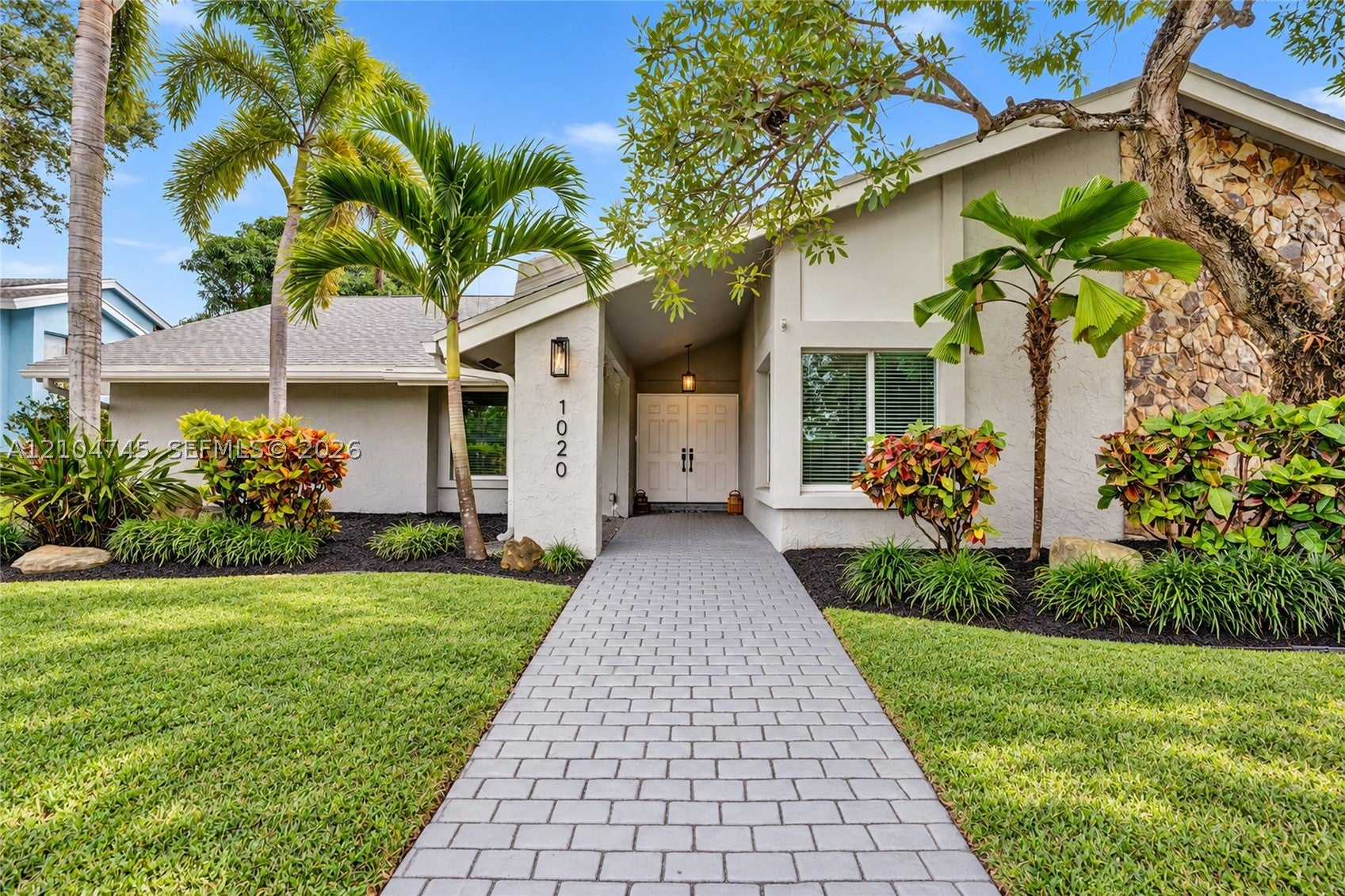 Front of the one-story home with a paver walkway and tropical landscaping