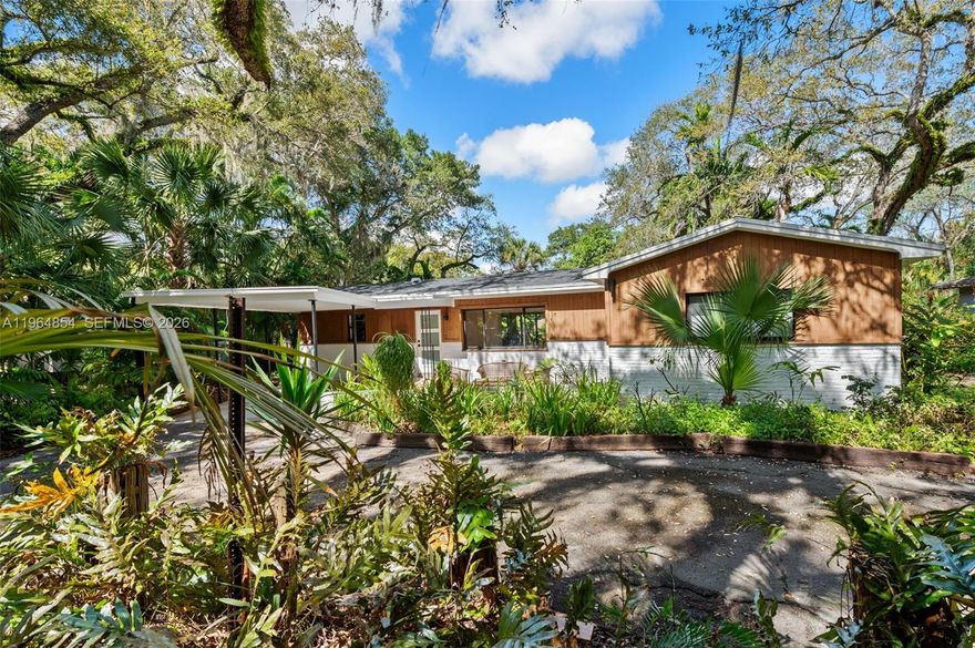 Welcome to 1745 Ne 137th Ter a charming 3 bedroom 2 bath Mid-Century Modern home w carport, tucked beneath a lush tree canopy on one of the area's most enchanting streets.  Arrive home each day by driving down this welcoming, nature-lined road, where mature trees create a peaceful setting coming & going. Step inside to a light-filled living room that immediately draws you outdoors through the picturesque rear windows.  The open floor plan, complemented by large impact windows & doors, seamlessly connects the interior to the surrounding greenery, creating a bright & inspiring atmosphere. The home features a spacious kitchen w rich wood cabinetry, a premium Wolf refrigerator & Whirlpool stove & dishwasher, offering both style & function for everyday living & entertaining. Designed w a split-bedroom layout, 2 bedrooms & 1 bath are positioned just off the entryway, while a private 3rd bedroom & bath are set apart off the back living space, ideal for guests, a home office, or a tranquil primary retreat. Glass sliding doors open to a spacious covered patio, ready for your outdoor living room, dining space, or creative garden design - all embraced by nature. A charming front patio, shaded by grand trees, offers another serene spot to relax. Located in "Enchanted Place" known for its magical holiday light displays form December through January, this is more than a home, it's a lifestyle connected to the outdoors.  Call today & come experience it for yourself.