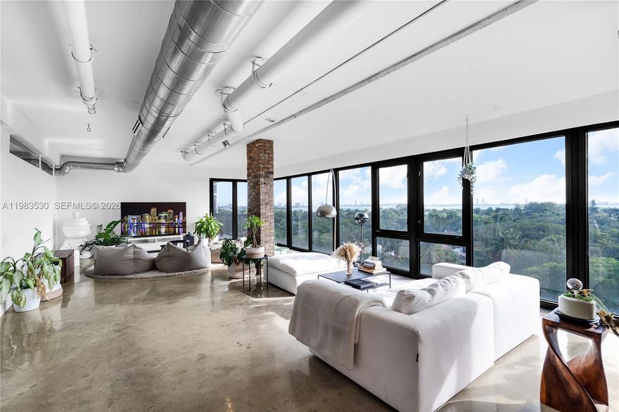 Discover this one-of-a-kind loft-style 4BD/3.5BA furnished residence—currently configured as a 3-bedroom plus storage—offering dramatic open-concept living, sweeping floor-to-ceiling glass, and panoramic views of Biscayne Bay, the Miami skyline, and lush tree canopies. Designed with an industrial-modern aesthetic, the home showcases exposed ducts, polished concrete floors, brick accents, and custom wood millwork throughout. The expansive great room seamlessly integrates living, dining, and an open chef’s kitchen, creating an ideal setting for entertaining. The primary suite delivers a true retreat with incredible natural light, oversized balcony access, and a sculptural soaking tub set against skyline vistas. Multiple lounging areas, flexible spaces perfect for office or creative use, and generous storage enhance daily living. The boutique building offers two elevators, just 3–4 residences per floor, a rooftop dry sauna, and pool, and is just a 3-minute walk from beautiful Morningside Park—offering an exceptional blend of volume, character, lifestyle, and location at the edge of Morningside and the MiMo District.