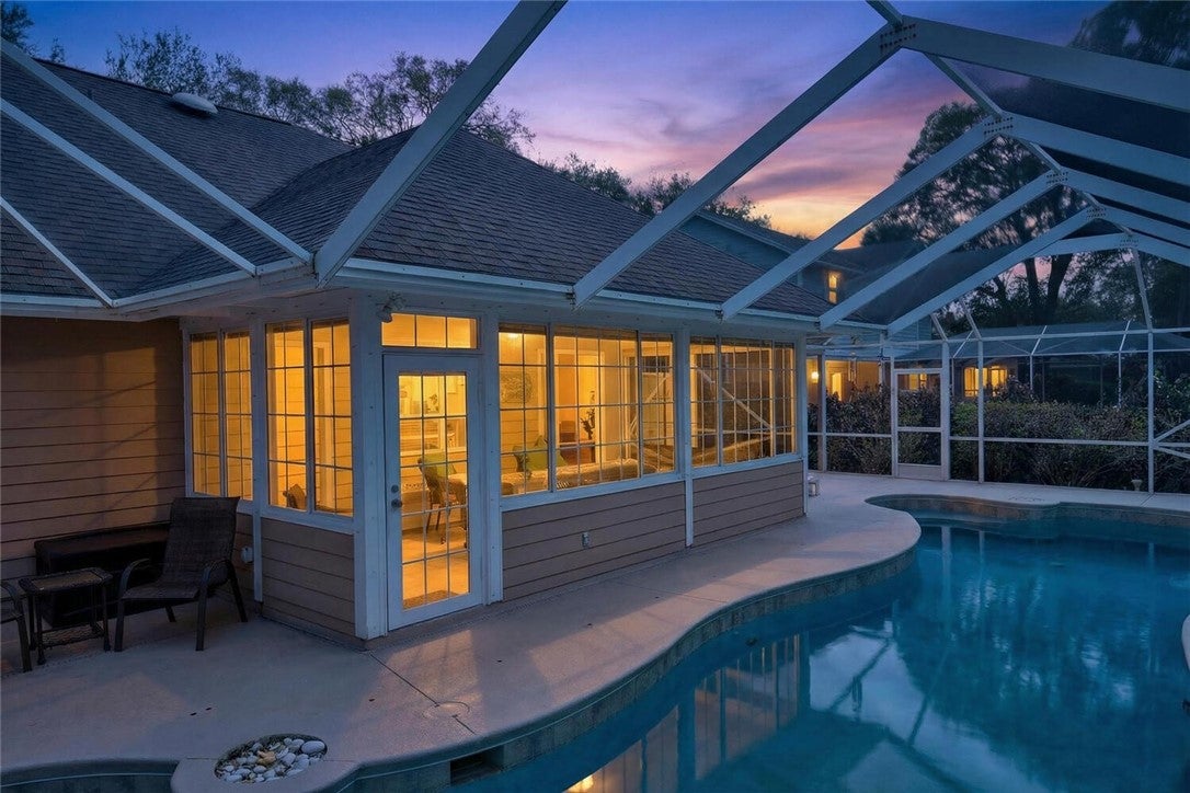 Pool at dusk featuring a sunroom, an outdoor pool, glass enclosure, and a patio