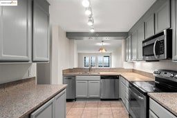 Kitchen featuring stainless steel appliances, gray cabinets, light stone counters, and hanging light fixtures