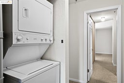 Laundry area with light colored carpet, estacked washer and dryer, and a textured wall