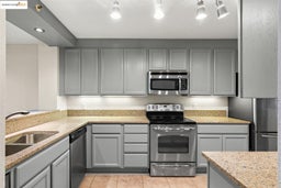 Kitchen with gray cabinets, appliances with stainless steel finishes, light stone counters, and light tile patterned floors