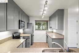 Kitchen with gray cabinetry, range with electric cooktop, light tile patterned floors, stainless steel microwave, and light stone counters