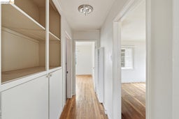 Hallway featuring built-in cabinetry with open shelving and closed storage, wood-finish flooring, and white walls