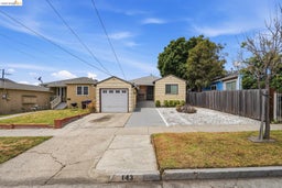 Single-story residence featuring a detached garage with a white panel door, a paved driveway, and a low-maintenance front yard with gravel and mature shrubbery