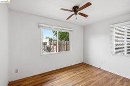 Room featuring wood-finish flooring, white walls, and a ceiling fan