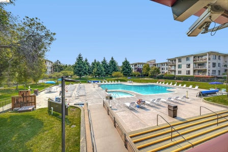 Expansive community pool area featuring a large swimming pool, a separate wading pool, a surrounding concrete deck, and multiple lounge chairs