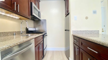 Kitchen featuring wood-finish cabinetry, stainless steel appliances, speckled countertops, and light wood-finish flooring