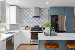 Kitchen with appliances with stainless steel finishes, wall chimney range hood, blue cabinets, a kitchen breakfast bar, and light stone countertops