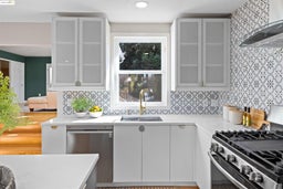 Kitchen featuring appliances with stainless steel finishes, light stone countertops, ventilation hood, white cabinetry, and glass insert cabinets