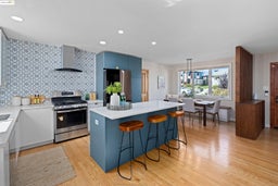 Kitchen with blue cabinetry, appliances with stainless steel finishes, a kitchen island, a kitchen breakfast bar, and wall chimney range hood