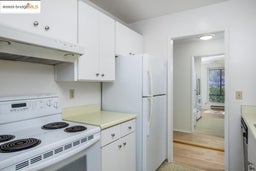 Kitchen with white appliances, under cabinet range hood, light wood finished floors, and white cabinets