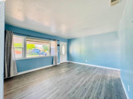 Spacious room featuring wood-finish flooring, a white entry door with an oval glass insert, and a large window