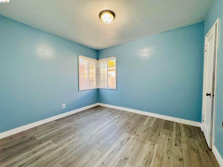Room featuring wood-finish flooring, light blue walls, and white baseboards