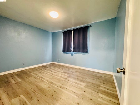 Room featuring wood-finish flooring, light blue walls, white baseboards, and a flush-mount ceiling light fixture