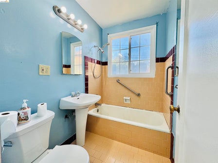 Bathroom featuring a pedestal sink, white bathtub, and tiled shower surround with a grab bar