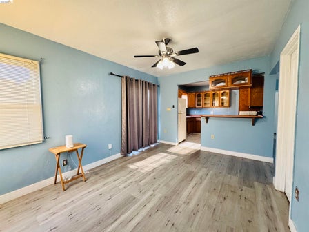 Open-concept living space featuring wood-finish flooring, a ceiling fan with integrated lighting, and a pass-through counter with overhead cabinetry