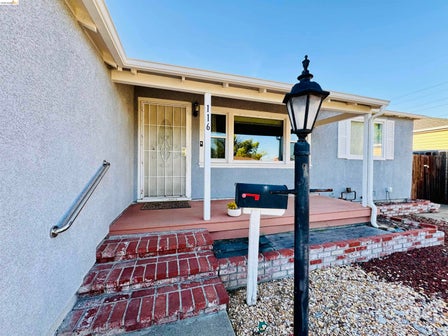 Front porch entry with a security screen door, red brick steps, and an exterior wall-mounted handrail