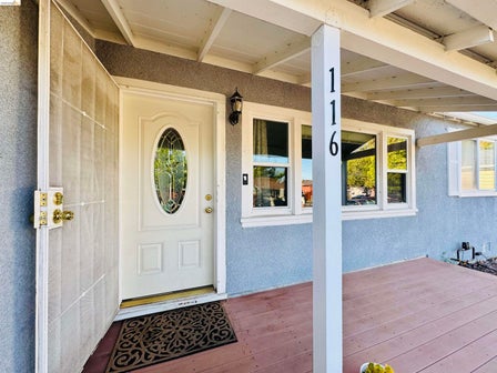 Front entry featuring a white door with an oval-paned window, a white security screen door, and a covered porch with wood-finish flooring