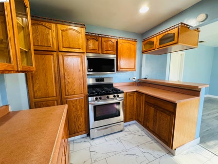 Kitchen featuring oak wood cabinetry, a stainless steel gas range, and a built-in microwave