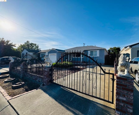 Gated property entrance featuring a wrought iron gate with decorative accents, brick columns, and stone lion sculptures