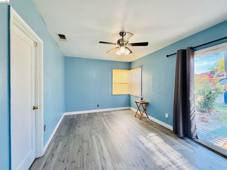Room featuring light blue walls, wood-finish flooring, a ceiling fan with integrated lighting, and a sliding glass door providing exterior access