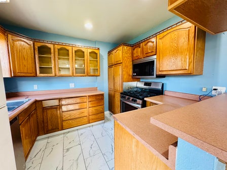 Kitchen featuring a gas range, over-the-range microwave, wood-finish cabinetry with some glass-front doors, and a double-tier counter space