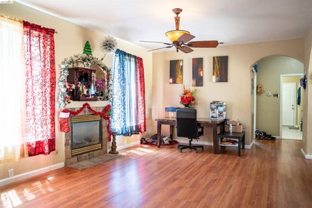 Living area featuring wood-finish flooring, a stone-surround fireplace, and an arched doorway