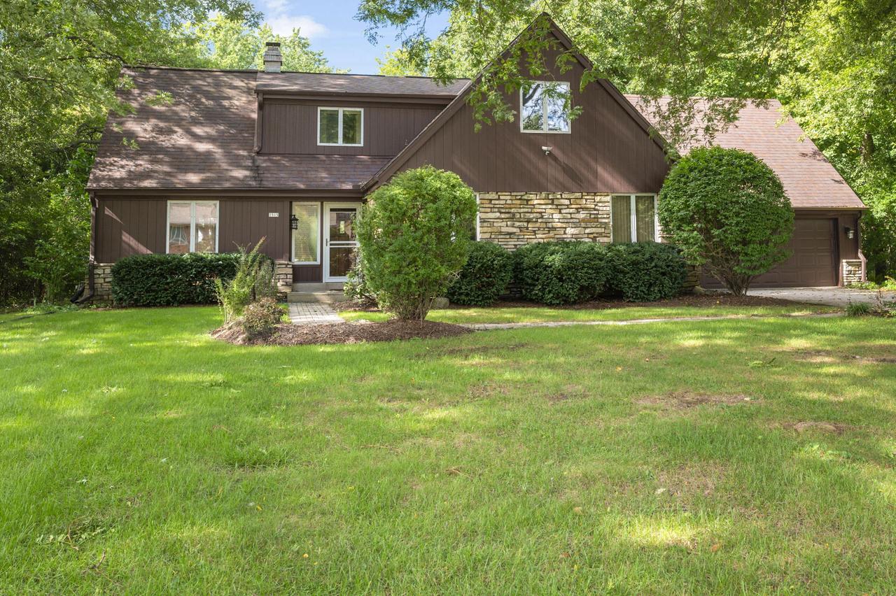 Brown two-story home with a stone facade, attached garage, and leafy trees around its broad lawn.