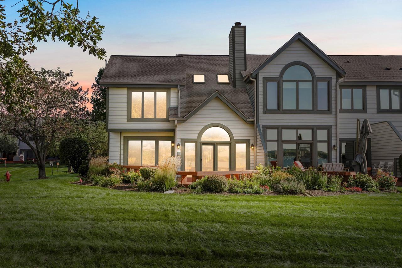 Large gray house with arched windows, wooden deck, and landscaped lawn at sunset.