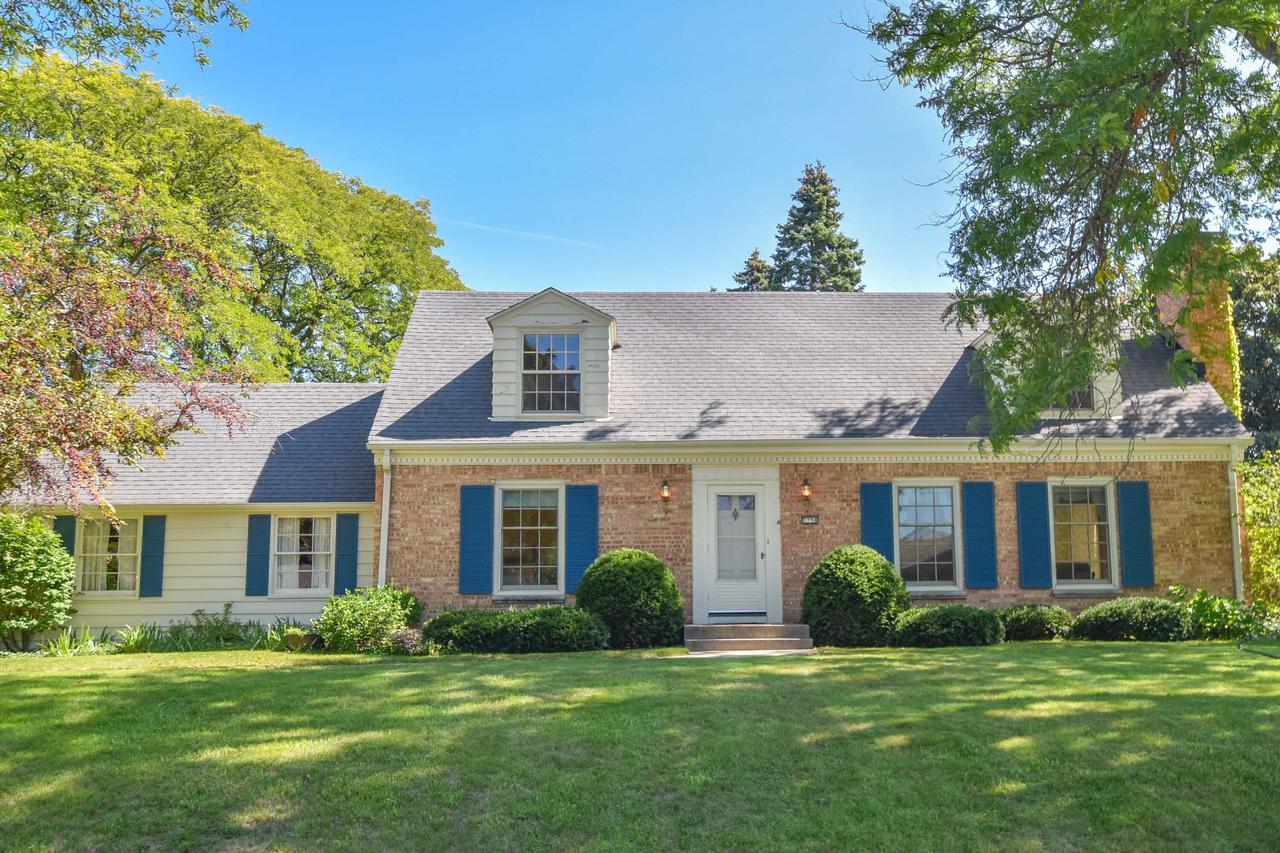 Brick-and-siding home with blue shutters, a dormer window, mature trees, and a broad lawn.