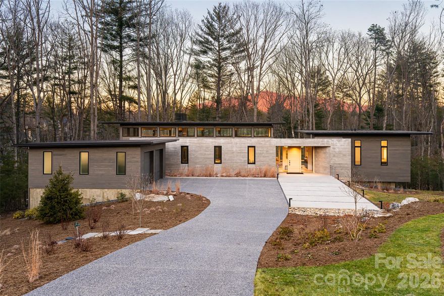 221 Fern Grove is a striking modern residence designed by Altura Architects and built by Jade Mountain Builders, in The Ramble Biltmore Forest, one of Asheville’s premier gated communities offering walking trails, a wellness center and quick access to shopping, dining and downtown Asheville. LEED Gold Certified, this home was thoughtfully designed with sustainability and efficiency at its core. Positioned meaningfully on .98 acre for privacy with a high-efficiency geothermal heating and cooling system, energy-saving appliances, Lutron lighting and carefully selected materials support a lifestyle focused on responsible living without sacrificing comfort. The exterior blends Accoya siding with board-formed concrete and sound deadening insulation creating a refined modern aesthetic that feels grounded and enduring. Inside, warmth meets architectural precision. The entry, office and kitchen feature beautifully detailed wood-paneled ceilings that create an inviting, intimate feel. These spaces open into a dramatic great room anchored by high clerestory windows and expansive floor-to-ceiling Marvin windows, filling the home with natural light throughout the day. The living and dining areas frame serene views of dense forest and a nearby walking path, offering a seamless connection to the surrounding landscape. An exceptional screened porch extends the living space outdoors, finished with durable TimberTech flooring, the space combines low maintenance with clean, refined look that complements the home’s modern design. Just beyond, an adjacent deck features a built-in Coyote gas grill, creating an ideal setup for outdoor cooking and entertaining. The home features four spacious en-suite bedrooms, offering comfort and privacy for residents and guests. Every sightline was intentionally designed to bring in the outdoors, reinforcing a sense of calm and privacy. 221 Fern Grove is more than a home. It is a modern sanctuary that balances architectural integrity, environmental responsibility and everyday livability, an opportunity to enjoy refined design in harmony with nature.