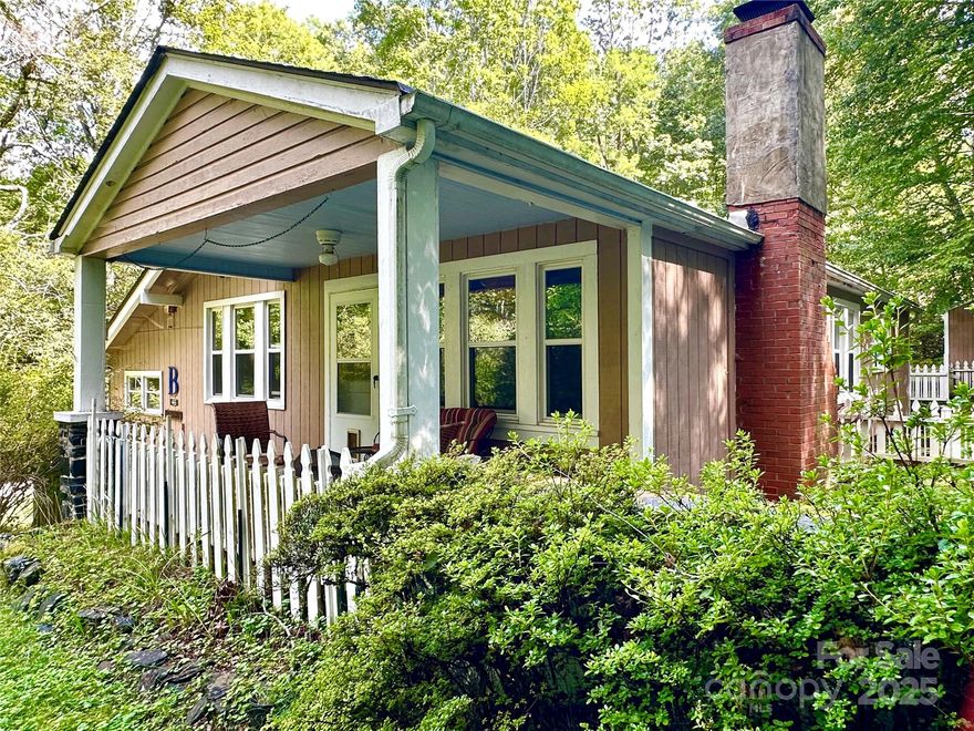 Large multi-pane windows with wooden blinds that invite natural light and offer serene views of the wooded surroundings. Neutral carpeting for softness and a ceiling fan with integrated lighting for functional, vintage-inspired comfort. The living room flows seamlessly into the adjacent dining area through a wide arched doorway, a subtle nod to early American cottage revival influences, creating an open yet intimate floor plan. The classic dining room features a warm, rustic design with vertical knotty pine walls that enhance its cabin-like charm. Matching cabinetry includes a built-in hutch with glass doors for displaying decorative items and glassware, plus solid drawers and cabinets below for storage. The cabinetry’s classic, slightly distressed finish with simple hardware adds to the rustic appeal, blending functionality with homely warmth.The thoughtfully designed kitchen balances elegance and convenience. Striking black raised-panel cabinetry with brushed nickel hardware contrasts beautifully with neutral tile flooring and soft wall tones. Ample storage is provided by cabinets above and below the durable laminate countertops, which mimic natural stone for a clean, cohesive look. A wide double window brightens the space, while coordinating black appliances, including a dishwasher and refrigerator, ensure a seamless aesthetic. Practical ceramic tile flooring in a neutral tone simplifies maintenance.Two well-sized bedrooms share a cohesive rustic and cozy aesthetic, blending natural wood elements with a warm, inviting atmosphere. Enjoy morning coffee on the covered front porch, host backyard BBQs or simply unwind to the soothing sounds of a gentle mountain stream flowing nearby. Easy year-round access, minutes to fine dining, the Blue Ridge Parkway and outdoor adventures; An ideal home for full-time residence, weekend getaway or vacation rental. A rare opportunity to own a slice of tranquility in the mountains. —schedule your private showing today!