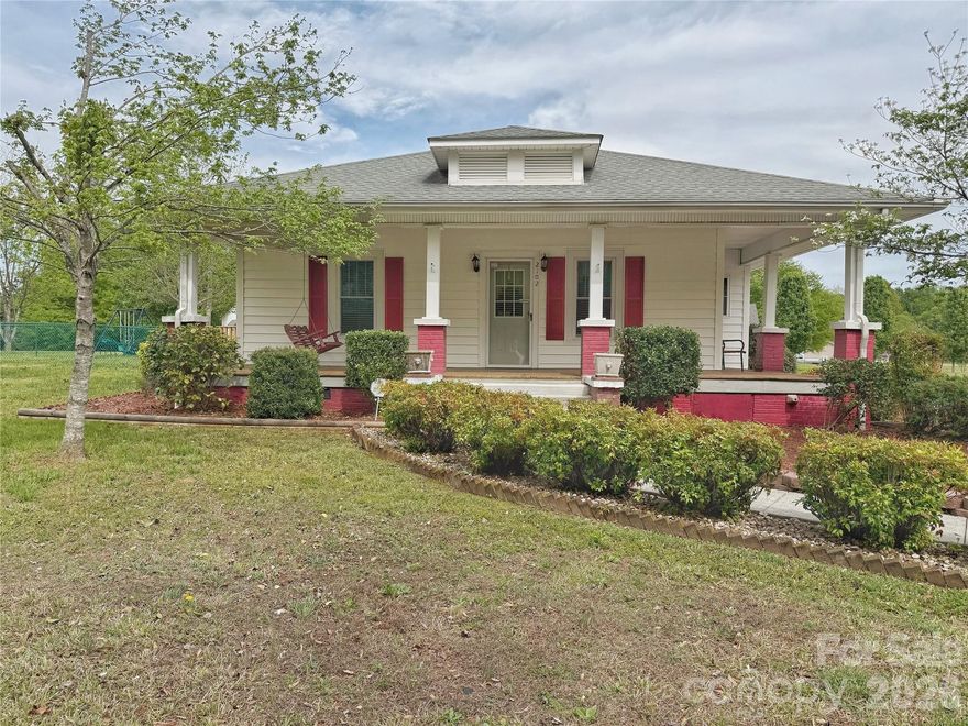 Rare opportunity to own a character-filled home on nearly an acre just outside Gastonia. This charming older home is full of character and situated on a beautiful, flat lot with mature trees and a peaceful setting.

Inside, the home features high ceilings, original architectural details, and wood flooring throughout much of the home. Spacious bedrooms and a traditional central hallway layout offer a functional floor plan, while the cozy den provides a comfortable gathering space. The home has strong bones and, while it offers an opportunity for updates, it is move-in ready as it sits.

Outdoor living is a standout feature, with a wraparound front porch, a deck off the dining area, and a large covered entertaining space adjacent to the carport—perfect for gatherings. The property also offers ample parking in addition to the attached carport.

The large, level lot provides plenty of space for outdoor activities, gardening, or hobbies, and includes multiple outbuildings for additional storage or workspace. A Generac generator is also included, adding peace of mind.

Located outside city limits, this property offers the benefit of no city taxes while still being convenient to Gastonia and surrounding areas.