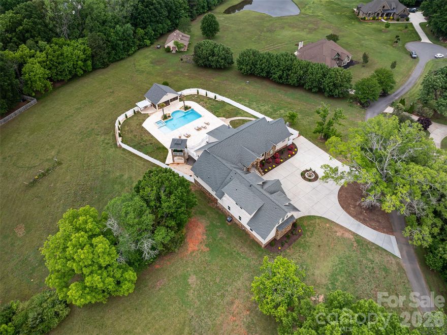 AMAZING nearly 10,000-square-foot custom home on 5 private acres — an extremely rare find! This recently built and beautifully upgraded estate truly has it all. Conveniently located in Waxhaw near Wesley Chapel, the property offers the perfect combination of privacy, luxury, and convenience. The expansive five-acre lot gives you endless possibilities — enjoy the peaceful green space as-is, build an additional structure, add a barn, create recreational areas, or simply enjoy the privacy and room to spread out.

Built in 2019, the home was thoughtfully customized by the builder with elevated design details and high-end finishes throughout. The light-filled floor plan was designed for both everyday living and entertaining on a grand scale, while still feeling warm and inviting.

The main level opens into a stunning foyer leading to the impressive living room with soaring vaulted ceilings, oversized windows, and a beautiful double-sided fireplace. The open flow connects seamlessly to the office, dining room, breakfast area, and incredible chef’s kitchen. The kitchen offers everything you could need, including extensive cabinetry, high-end appliances, and a large walk-in pantry.

The primary suite on the main level is its own private retreat, featuring a fireplace, sitting area, private access to the back balcony, and an oversized spa-like bathroom with a large walk-in shower. The massive six-car garage easily accommodates car collections, recreational vehicles, storage, and more, and opens conveniently into a functional mudroom/drop zone area.

Upstairs features spacious secondary bedrooms and bathrooms, along with additional flexible living space perfect for a bonus room, playroom, media room, or lounge area.

The fully finished basement is an entertainer’s dream. It includes a second kitchen with bar seating, a large open living and game room with fireplace, a gym, movie theater room, and additional bedrooms and bathrooms ideal for hosting guests or extended family.

The outdoor living spaces are truly the highlight of this incredible property. Multiple covered and uncovered patios provide endless areas for entertaining, dining, relaxing, and enjoying the beautiful surroundings. The resort-style pool and hot tub feature custom waterfall details and lighting, creating an unbelievable backyard experience. The expansive pool area offers ample space for large gatherings while still maintaining complete privacy.

There is also a stunning pool house featuring a screened-in living area, outdoor kitchen, fireplace, covered lounge space, and bathroom — the perfect extension of the home for year-round enjoyment.

The main home and pool area are fully fenced with privacy fencing for security and peace of mind, while the remaining acreage beyond offers endless opportunity and flexibility to make the property your own.

This is truly a little slice of heaven just outside the hustle and bustle of Charlotte — a rare opportunity to own an incredible luxury estate with acreage, privacy, and every amenity imaginable.