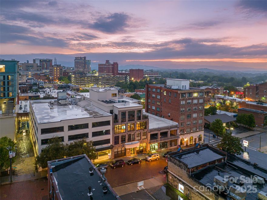 Breathtaking Luxury Penthouse in Downtown Asheville! Discover city living at its finest with modern elegance and convenience in this extraordinary 4th-floor residence, perfectly blending period architectural details with contemporary sophistication. Situated at a prestigious Downtown Asheville address along the city’s oldest brick roads, this boutique luxury penthouse is set within a historic 1923 building and showcases original 100-year-old hardwood floors, soaring industrial-height ceilings, reclaimed brick, wood accent walls, and expansive windows framing spectacular panoramic mountain vistas and gorgeous city skyline views.

This grandly appointed and fully furnished 4 bedroom, 3.5 bath home offers a spacious layout that balances timeless character with modern functionality. The west-facing exposures open to a 243.6 sq ft private terrace, extending the living experience outdoors—perfect for entertaining guests, enjoying astronomical events, or embracing the beauty of the mountains. The elegant primary suite features a spa-inspired bathroom and a custom designed walk-in closet for both style and function. Two additional bedrooms include private luxury baths and, for privacy, are located on the east side of the floor plan, while the fourth bedroom offers flexibility as an office, yoga/exercise, or meditation room.

At the heart of the home, the sleek, open chef’s kitchen is custom designed for both entertaining and mastering the culinary arts, featuring Wolf and Sub-Zero appliances, unified storage solutions, custom cabinetry, and refined finishes. Every detail has been thoughtfully curated, ensuring that every element is designed for both function and modern elegance.

Additional highlights include deeded secured underground parking, pre-wired for EV charging, offering both convenience and peace of mind. Residents also enjoy exclusive access to a spectacular rooftop terrace with lounge seating, an indoor fireplace, and an outdoor fire pit—the perfect setting to gather with family and friends while savoring Asheville’s unforgettable sunsets and long-range vistas.

Beyond the residence itself, the location defines refined city living with unmatched convenience. Step outside your front door and walk to Asheville’s vibrant arts scene, award-winning restaurants, boutique shopping, galleries, and cultural attractions. All of downtown’s best amenities are just a short stroll away, allowing you to experience the dynamic spirit of the city while enjoying the privacy, space, and luxury of your own penthouse retreat.

This remarkable penthouse offers a rare opportunity to own a piece of Asheville history while enjoying modern luxuries and breathtaking views. A truly one-of-a-kind home that seamlessly blends historic charm, modern sophistication, and world-class design—an unparalleled residence in the heart of vibrant Downtown Asheville.