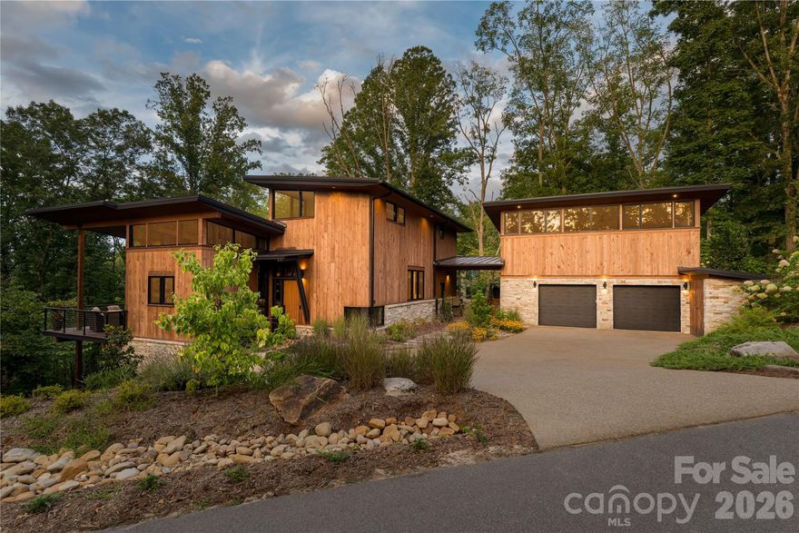 Tucked into the trees in the sought-after community of Olivette, this custom mountain modern home by Jade Mountain Builders is a seamless blend of architectural design, craftsmanship, smart technology and natural beauty.

Striking rooflines, warm wood siding, stacked stone accents, and dramatic walls of glass create a bold architectural statement. Inside, refined finishes and intentional details define every space.

The main living area is framed by expansive windows that capture the surrounding forest, filling the home with light and an ever-present connection to nature. In the winter months, enjoy views and sounds of the French Broad River shimmering through the trees—a rare and peaceful seasonal bonus. A stunning custom built-in shelving wall anchors the space, offering both artistry and function.

The chef’s kitchen is a modern showpiece—sleek black cabinetry, rich wood accents, exposed beams, and polished concrete floors with radiant heat for added comfort. A generous island invites gathering and conversation, blending sophistication with warmth in true mountain modern style.

Above the garage, a full luxury studio apartment offers exceptional flexibility—perfect for guests, extended family, rental income, or a private home office. Thoughtfully designed and beautifully finished, it mirrors the quality and aesthetic of the main residence.

Outdoor living is equally compelling, with covered terraces and elevated balconies designed to immerse you in the peaceful wooded setting. Or enjoy hanging out in the backyard down by the firepit. There is also a fenced in side yard for your 4-legged companion animal.

And then there’s Olivette.

Set along the French Broad River, this one-of-a-kind community offers river frontage, vineyards, a working community farm, miles of walking and biking trails, a dog park, and acres of preserved green space. Just minutes from Asheville, yet worlds away, Olivette is known for its architectural integrity, sustainability, and vibrant sense of community.

This is more than a home.
It’s refined mountain living.

Furnishings are negotiable.