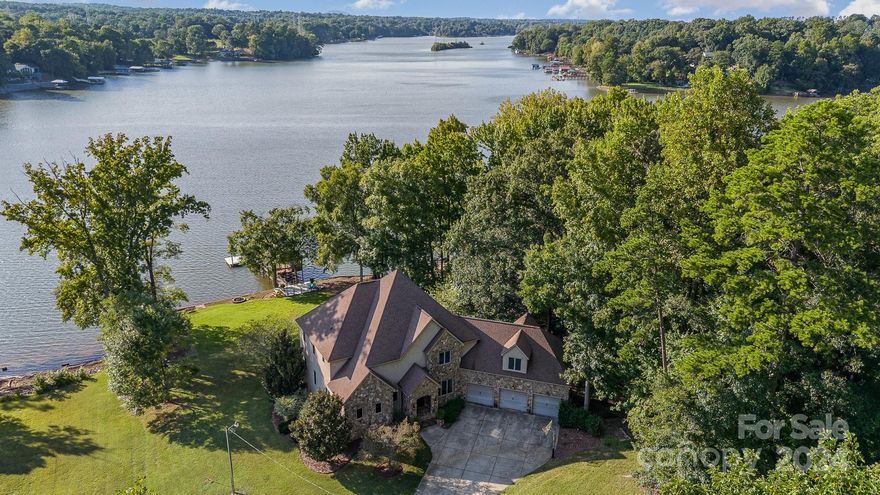 Welcome to this exquisite waterfront residence on the Catawba coast of Lake Wylie—private & serene lake life with stunning Carolina sunsets. Covering over 6,800 sqft on 1.3 acres with nearly 350 feet of pristine shoreline, this property offers abundant space for living and relaxation. The main level includes the primary suite, opening to a vaulted living area with coffered ceilings and access to a patio overlooking the water. Upstairs are three bedrooms with ensuites and walk-in closets, plus a bonus room above the three-car garage. The basement features a bar, guest suite, additional living space, gym/yoga studio, and storage. Glass doors lead to a patio and lawn, perfect for leisure or play, with room for a football field or pool. Just over a mile from the new River District Development, this home is 15 minutes from the airport and 25 minutes to uptown, offering convenience and tranquility. This waterfront haven invites you to enjoy luxury, privacy, and the best of Carolina living.