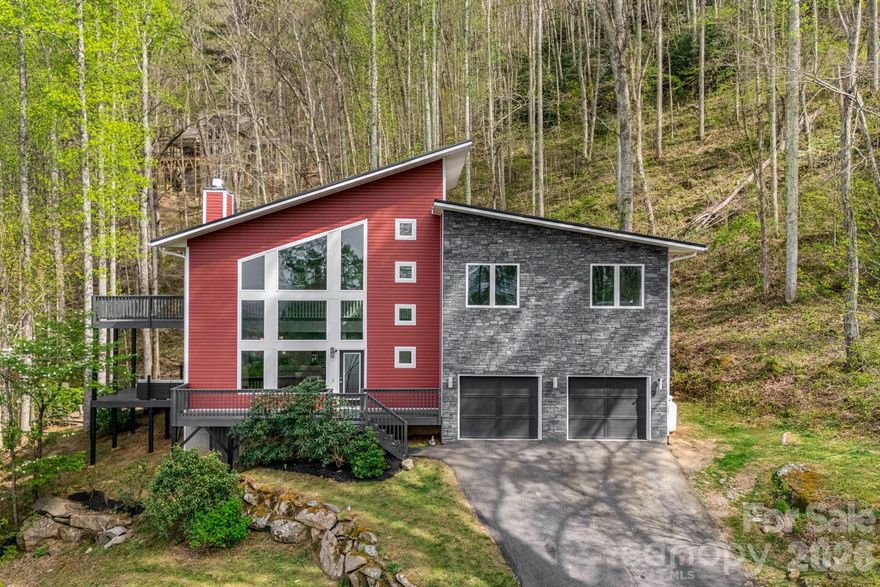 Defined by its modern skillion rooflines and soaring interior volume, this architecturally distinctive contemporary home offers an elevated take on mountain living, set on 2.18 private, wooded acres with a flowing stream and fire pit. The main living space rises to nearly two-and-a-half stories at its peak, creating a light-filled, open atmosphere that feels both expansive and inviting.
At the heart of the home, a dramatic floor-to-ceiling black stone fireplace anchors the living room, while expansive windows and multiple vantage points frame long-range mountain views. The open-concept kitchen features quartz countertops and flows seamlessly into the dining and living areas—ideal for both everyday living and entertaining.
The home offers 4 bedrooms plus an office, with a well-considered layout that balances privacy and flexibility. The upper level includes the primary suite—featuring a custom tile shower with dual shower heads—along with two additional bedrooms, each with its own bath. A fourth bedroom on the lower level also includes an ensuite bath, providing comfortable accommodations for guests. Fresh interior paint throughout and new carpet on the upper level add to the home’s move-in-ready appeal.
A spacious loft overlooking the main living area creates a versatile secondary living space and opens to an upper-level deck, where mountain views continue to take center stage. Outdoor living is equally inviting, with both main-level and upper-level decks designed to take full advantage of the surrounding landscape.
With its unique architectural presence, serene natural setting, and multiple indoor and outdoor living spaces, this is a rare opportunity to experience elevated mountain living just minutes from everyday conveniences.
