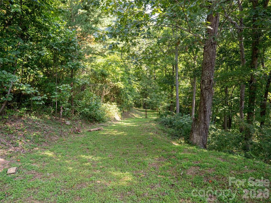 Relaxed and easy-build home site gently tucked into the woods of Reynolds Mountain in North Asheville. This softly sloped lot offers meaningful savings on building costs compared to steeper mountain parcels, allowing for a more straightforward foundation, driveway, and utility installation. The property borders a 16-acre wooded conservation area with access to a one-mile nature trail, creating a private, natural setting that feels secluded while remaining close to everyday conveniences. A gentle drive leads down into a quiet, tailored woodland environment—ideal for a home immersed in nature without sacrificing accessibility. Reynolds Mountain is one of North Asheville’s premier mountain-top neighborhoods, offering a rare balance of privacy and walkability. Enjoy easy access to Beaver Lake and the shops and services of Reynolds Village, all just minutes from home. Downtown Asheville is less than 10 minutes away. City water, city sewer, natural gas, and electric are already in place and underground, simplifying the building process. A well-positioned lot that combines natural beauty, practical infrastructure, and long-term value—ready for your vision. Surveys attached to listing.