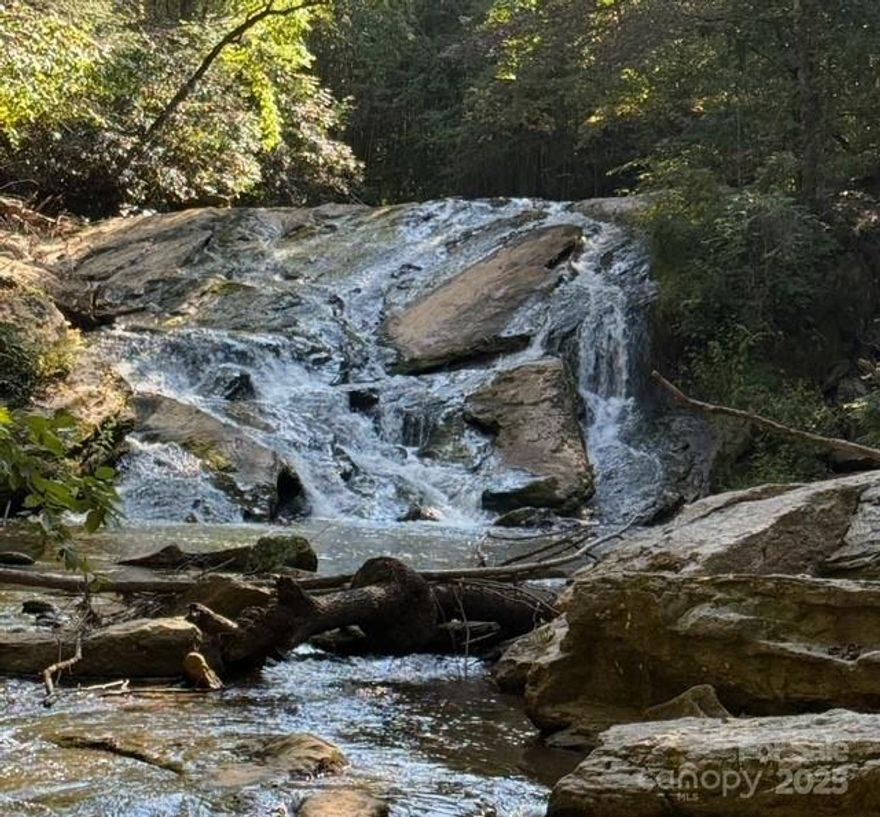 Your Own Slice of Carolina Magic

Step into a place where nature does all the talking. Tucked away in the heart of the mountains, this rare piece of land is unlike anything else on the market. With a sparkling waterfall cascading through the property and a U-shaped river that flows in and out, it feels like your very own enchanted kingdom. In the middle, you’ll find a dreamy stretch of land perfect for stargazing, camping, or maybe one day building your forever escape on the higher ridges, safe from potential flooding and with views worth every step.

On the Land

A rustic off-grid camping cabin rests quietly among the trees. It was built for weekends, not forever, complete with an old outhouse but it sets the scene for wilderness adventures. The cabin itself holds no value in this sale, but it whispers of the stories already lived here.

An aged pump house once served RV hookups. It’s been years since it worked, and it will need repair, but it still hints at possibility.

A septic tank is in place, with a report pending.

Powerlines run along the side of the front of the property, but don’t let that discourage you. Once you’re on the land, you can’t even see them.

The well situation is uncertain given the rocky ground beneath, another reason this land favors those with vision and imagination.

Why You’ll Love It

This is land for dreamers, explorers, and anyone who knows that places of peace are priceless. Whether you envision a hideaway in the high spots, weekends by the river, or just want to say you own land where waterfalls sing you’ll find that here.

Important Note

Please remember: showings are by appointment with a real estate agent only. Do not go chasing waterfalls on your own! Trespassing is not permitted, and you must be accompanied to enter.

The Bottom Line

With water, nature, and space to build your dreams, this property is as magical as it is rare. Bring your boots, bring your vision, and let your imagination flow like the river that runs through it.