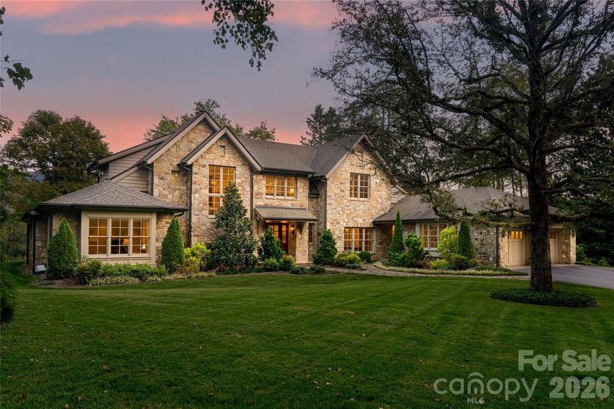 Set along the 13th fairway of the private Biltmore Forest Country Club, this quietly commanding mountain estate is a study in craftsmanship, privacy and enduring elegance. Reached by a long, gently rising drive through mature trees, the home reveals itself on a flat, sunlit 1.71-acre homesite, where sweeping golf course and mountain views unfold with effortless grace. Designed by PLATT Architecture and built between 2017 and 2019, the stone residence offers approximately 5,000 square feet of finished living space across two levels, with an additional 3,500-square-foot lower level plumbed and planned for future expansion. The architecture is timeless yet forward-looking, Energy Star certified, geothermal heated and cooled, and supported by a whole-house generator, delivering modern performance without compromising aesthetic integrity. Inside, light and volume define the experience. Ten-foot ceilings on the main level rise to vaulted 12-foot ceilings above, while wide-plank solid oak floors, substantial millwork, and Ashley Norton bronze hardware establish a refined, tactile warmth. The great room, with its soaring beamed ceiling, stone fireplace and bespoke cabinetry, opens through French doors to an expansive stone terrace, nearly 50 feet in length, designed for seamless indoor-outdoor living against a backdrop of mountains and fairways. The main-level primary suite is a private sanctuary, offering terrace access, panoramic views, heated marble floors and dual dressing rooms with custom quarter-sawn oak cabinetry. Additional bedroom suites, one more on the main level and three above, including a second primary suite, provide exceptional flexibility for guests or multi-generational living, each with beautifully appointed marble baths and abundant natural light. At the heart of the home, the gourmet kitchen pairs custom Mason Elliott cabinetry with Brazilian granite, professional-grade appliances and a gracious breakfast area overlooking the landscape. It opens to a skylit screened porch with stone fireplace and built-in grill, an all-season retreat equally suited to intimate mornings or elegant evenings. Every detail has been considered, from the home elevator and advanced water filtration to curated lighting, integrated audio and thoughtfully designed service spaces. This is a residence of quiet confidence, where luxury is measured not by excess but by intention.