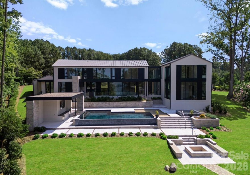 Completed in 2025, this Lake Norman modern masterpiece is set on 1.45 gated acres, offering rare privacy and sweeping lake views. Elegantly designed for waterfront living, the home combines architectural sophistication with resort-style amenities, just minutes from Trump National Golf Club and a short drive to Mooresville’s premier dining, shopping, and amenities.

A dramatic two-story foyer welcomes you through a striking 10-foot solid oak pivot door, immediately framing sweeping lake views beyond. The open-concept main level is anchored by 10-inch-wide white oak hardwood floors and walls of floor-to-ceiling windows that flood the home with natural light. The chef’s kitchen is a true showpiece, featuring an oversized Taj Mahal quartzite island, floor-to-ceiling soft-close cabinetry, hidden paneled Bosch appliances, and a breakfast nook with custom built-in storage. A beautifully appointed scullery provides additional prep space, a spacious walk-in pantry, secondary appliances, and seamless access to the outdoor patio for effortless indoor-outdoor living. The living and dining areas flow seamlessly from the kitchen, ideal for intimate gatherings and larger-scale entertaining, with the living room anchored by a sleek modern gas fireplace.

Privately located on the main level, the primary suite serves as a serene retreat with expansive lake views, a gas fireplace, and a custom walk-in closet featuring a center island, custom jewelry drawers, and integrated LED lighting. The spa-inspired bath offers a soaking tub, oversized walk-in shower, and elegant stone finishes. Also on the main level is a flexible office or guest suite, complete with corner floor-to-ceiling windows, double-door closet, and a full bathroom.

Upstairs, three spacious guest suites each feature ensuite baths and stunning lake views, complemented by a generous bonus media room, a glass-enclosed office or exercise space, an oversized laundry room, and an additional powder room.

Outdoors, enjoy true resort-style living with a vanishing-edge pool featuring a swim-up bar, spa, fire pit, and outdoor kitchen, all complemented by a poolside structure with a 100-inch TV and bathroom. White stone walkways lead to a private lakefront beach and dock, offering four seasons of exceptional Lake Norman living. A three-car garage with sleek dark glass-paneled doors provides direct access to the drop zone and exterior, along with built-in cabinetry and ample storage for everyday convenience.

With its curated designer finishes, striking modern organic architectural features, unmatched resort-style amenities, and exceptional privacy, this sophisticated waterfront property is a true standout on Lake Norman.