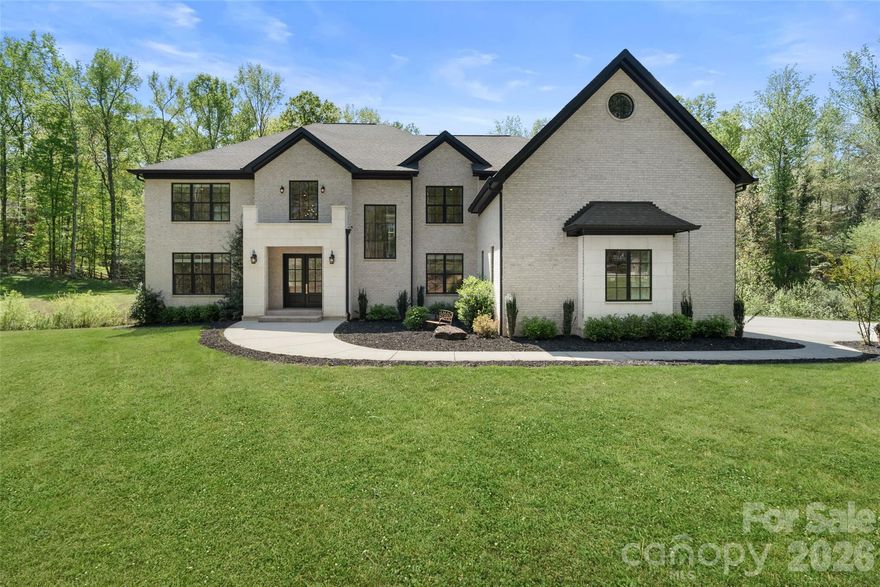 Stunning 4-bedroom, 5.5-bath custom Weddington home offering 5,502 sq ft of refined living on nearly 2 private acres. Features include a massive 4-stall garage with bonus room above.
Double doors welcome you into a dramatic two-story grand foyer adorned with a designer chandelier, intricate custom millwork, and contemporary stairs leading to an elegant gallery landing. The foyer opens seamlessly to a sophisticated home office complete with built-in cabinetry. The rear-facing family room impresses with a gas fireplace, beamed ceilings, and a dramatic wall of glass featuring triple French doors that flood the space with natural light. This flows effortlessly into an oversized, entertainment-focused kitchen wrapped in Brazilian marble on every surface — including a prep island with sink and an expansive 10-foot multi-seat waterfall island. Chef-inspired appliances include a 48” Jenn-Air gas range with smart oven, pot filler faucet, custom range hood, full-size side-by-side refrigerator/freezer, and a hidden microwave tucked inside the walk-in scullery. Informal dining connects directly to a covered terrace with a wood-burning fireplace, creating the perfect setting for year-round entertaining. Additional conveniences include an oversized mudroom with a dedicated drop zone and pet station. Upstairs, the primary suite offers a gas fireplace with room for seating, a large walk-in closet with custom built-ins and a spa-like bath featuring an oversized glass-enclosed multi-head shower and a free-standing vessel tub. Throughout the home, 5” white oak flooring, tall ceilings, and custom millwork create a cohesive, elevated atmosphere. Located just minutes from vibrant Waverly shopping and dining, major highways including I-485, and some of the area’s highest-rated Weddington and Union County schools.